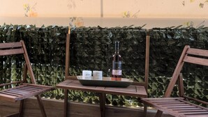 A wooden table with a bottle and glasses, two wooden chairs, and a wall with a floral pattern.