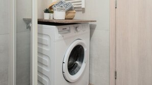A compact laundry room with a front-loading washing machine, a drying rack, and a wooden cabinet.