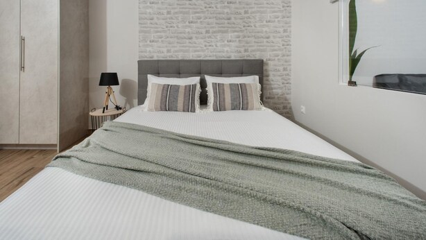 A bedroom with a bed, a nightstand, a lamp, and a window with a plant.