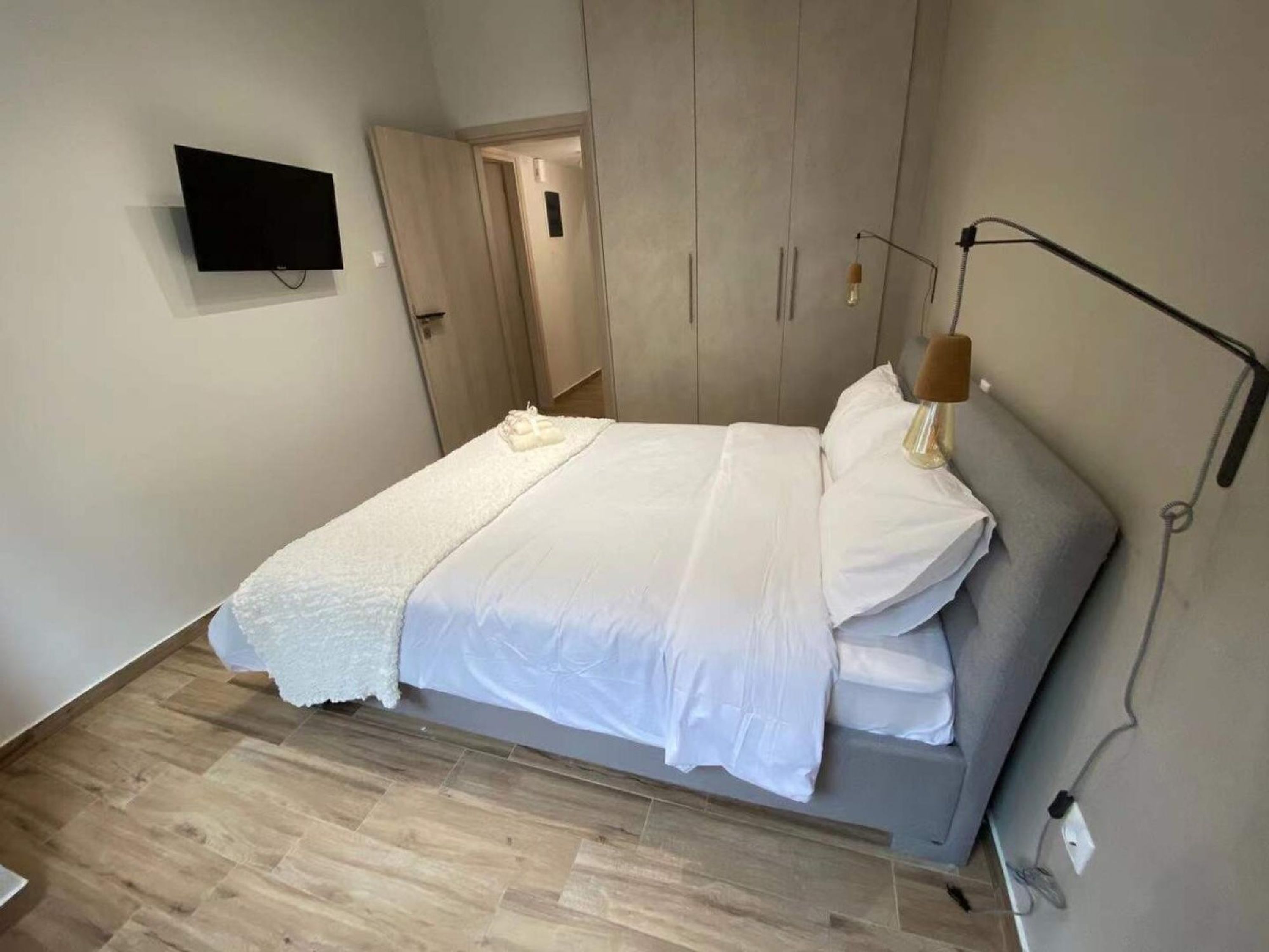 A bedroom with a bed, a TV mounted on the wall, and a bedside lamp.