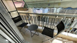 A balcony with a table and two chairs, a view of a building with clothes hanging on a line, and a metal railing. - Nature House - At093 (Athens)