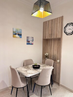 A dining area with a round table, four chairs, a decorative light fixture, and two wall-mounted clocks. - Nature House - At093 (Athens)