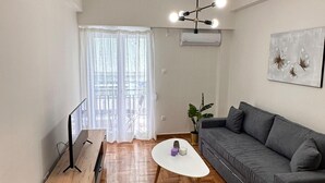 A modern living room with a herringbone wood floor, a grey sofa, a wooden coffee table, and a ceiling light fixture. - Nature House - At093 (Athens)