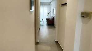 Un couloir étroit et bien éclairé, doté d’un sol carrelé, mène à un espace de vie comprenant un canapé et une table basse.