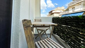Un balcon avec une table et des chaises en bois, un mur blanc à la texture particulière et une haie.
