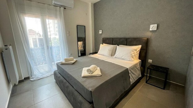 Une chambre moderne avec un grand lit, une petite table de chevet et une vue sur l’extérieur grâce à une porte-fenêtre coulissante.