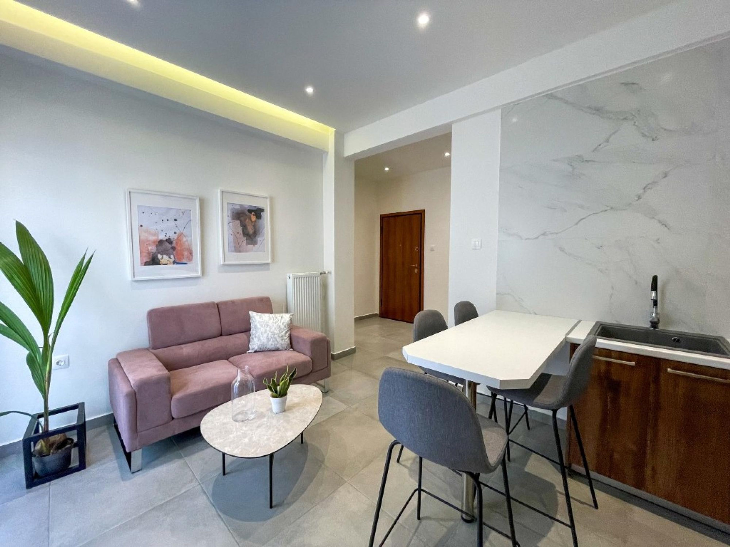 Un salon moderne comprenant un canapé, une table basse et des fauteuils, un coin repas avec une table et des chaises, et une cuisine équipée d’un évier et d’un plan de travail.