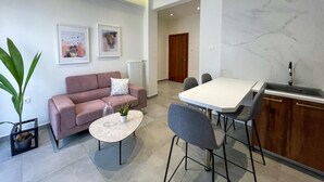 Un salon moderne comprenant un canapé, une table basse et des fauteuils, un coin repas avec une table et des chaises, et une cuisine équipée d’un évier et d’un plan de travail.