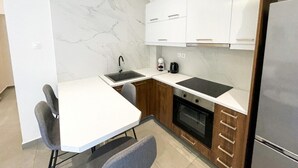 Une cuisine compacte avec des meubles blancs, un plan de travail noir, un évier, une machine à café et un four encastré.