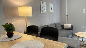 A modern living room with a sofa, two chairs, a coffee table, a lamp, and a potted plant. - Eunoia Apartment - At062 (Athens)