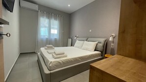 A modern bedroom with a bed, a wooden nightstand, a radiator, and a window with sheer curtains. - Eunoia Apartment - At062 (Athens)