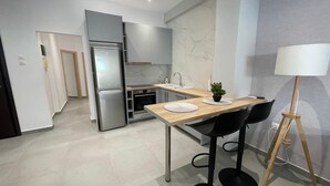 A modern kitchen with a built-in refrigerator, a sink, and a dining area with a table and chairs. - Eunoia Apartment - At062 (Athens)