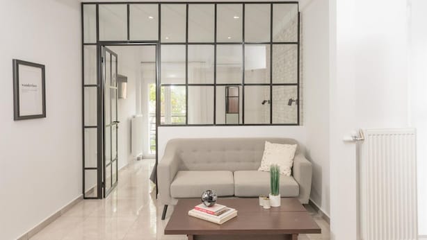 Una sala de estar moderna con un sofá, una mesa de centro con libros y un globo terráqueo, una puerta de vidrio que da a otra habitación y un radiador blanco.