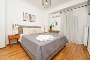 Ein ordentlich eingerichtetes Schlafzimmer mit einem großen Bett, Nachttischlampen, einem kleinen Nachttisch, einer Topfpflanze und einem Spiegel an der Wand.