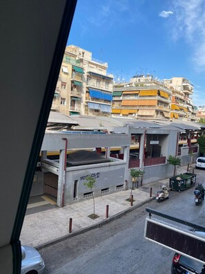 Een uitzicht op een meerlaags gebouw met balkons, een parkeerplaats met enkele geparkeerde scooters, en een helderblauwe lucht.