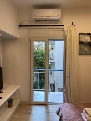 Een slaapkamer met een bed, een televisie, een kleine plant en een schuifdeur naar een balkon.