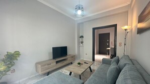 Una sala de estar moderna con un sofá gris, una mesa de centro de madera, un televisor sobre un mueble de madera y una planta en maceta.