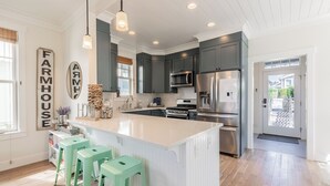 Une cuisine moderne dotée d’un grand îlot central, de meubles de couleur gris foncé, d’appareils électroménagers en acier inoxydable et d’une enseigne de style rustique.