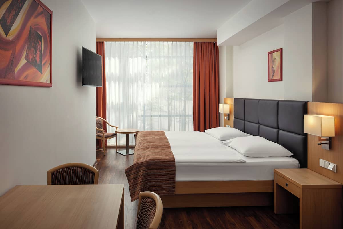 A hotel room with a bed, bedside table, lamp, chair, and a TV on the wall.