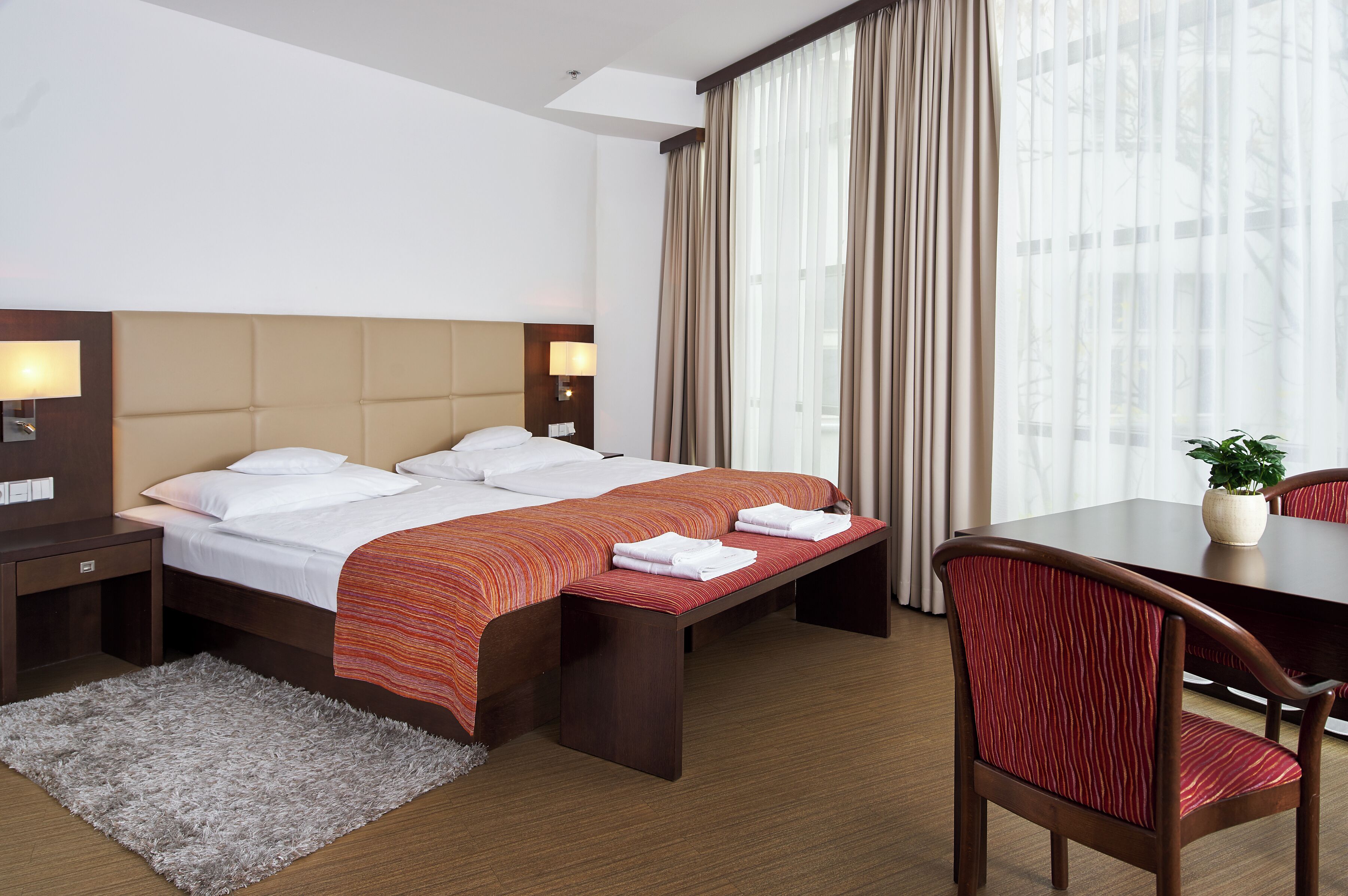 A hotel room with a bed, bedside tables, a desk, and a chair.