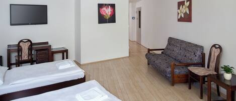 A hotel room with two beds, a sofa, a TV, and artwork on the walls.