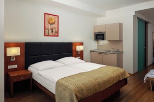 Quarto de hotel com uma cama, abajures, um quadro, uma kitchenette e uma porta verde.