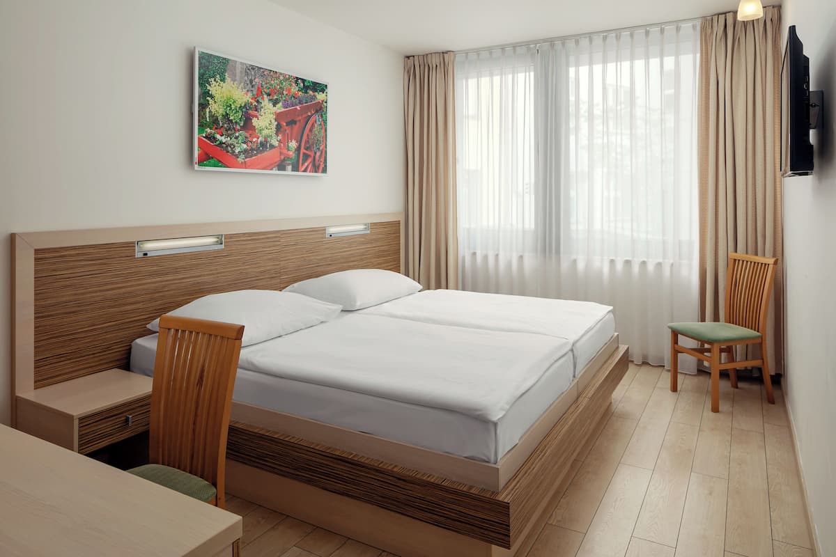 A hotel room with a wooden bed, a desk, a chair, a TV, and a window with curtains.
