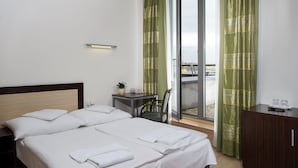 A hotel room with two beds, a small table with a plant, a desk with a phone, and a view of the outside through large windows. - Ankora Hotel Prague (Prague)