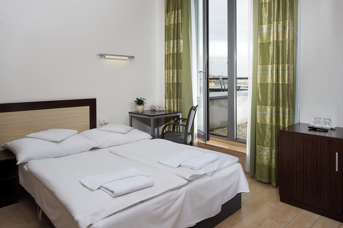 A hotel room with two beds, a small table with a plant, a desk with a phone, and a view of the outside through large windows.