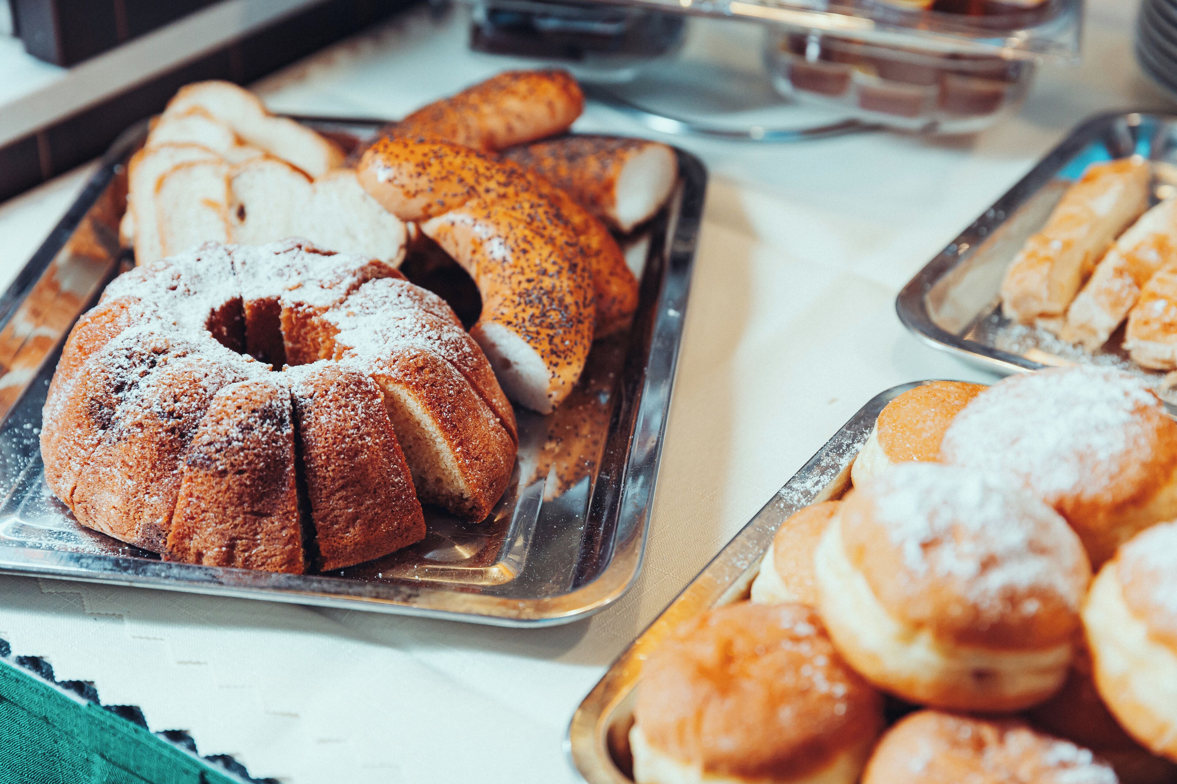 A buffet with various baked goods including a bundt cake, poppy seed rolls, and other pastries.
