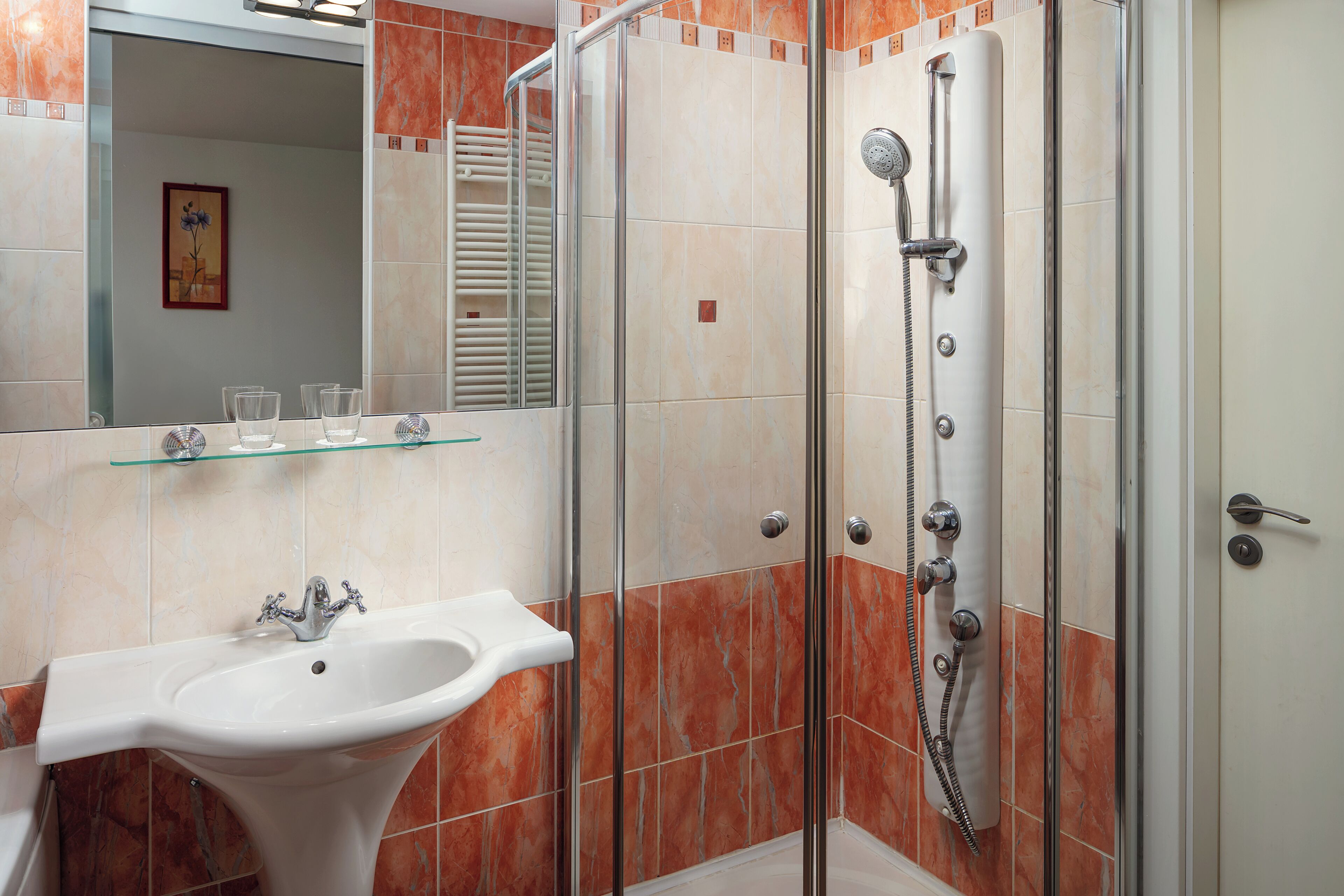 Un baño con ducha de vidrio, lavamanos pedestal y repisa de vidrio sobre el lavamanos.
