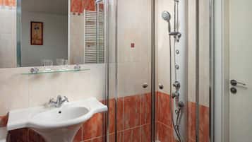 A bathroom with a glass-enclosed shower, a pedestal sink, and a glass shelf above the sink.