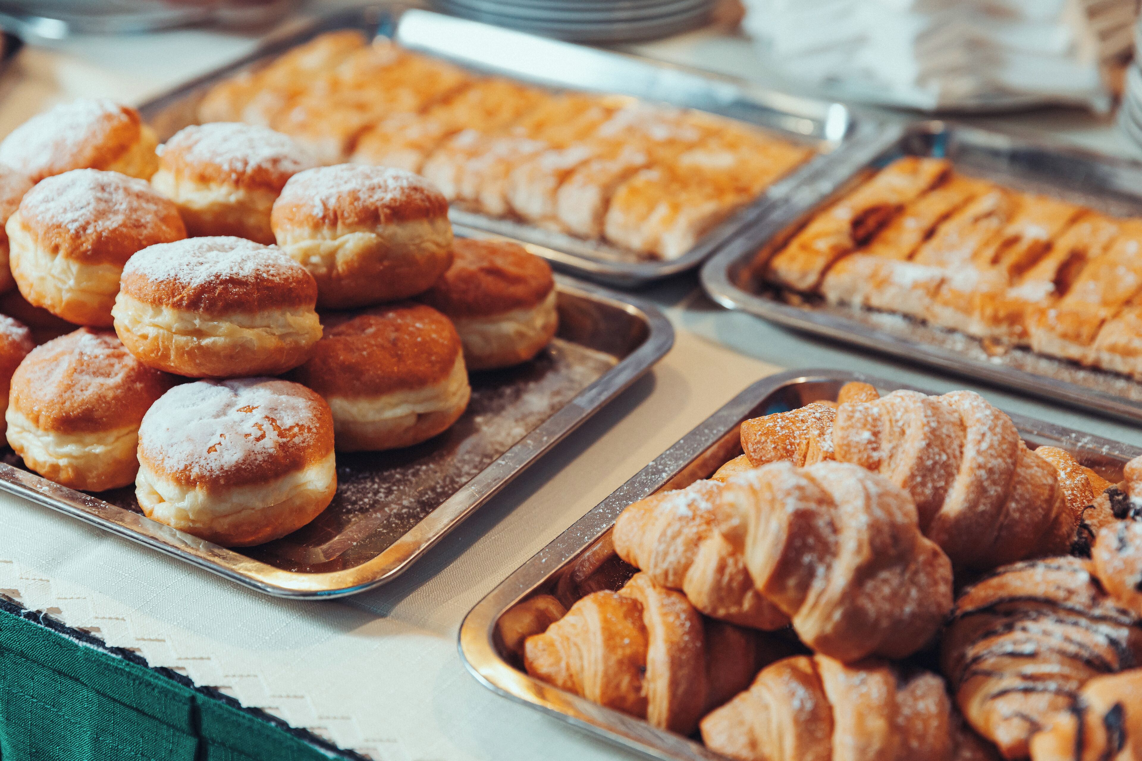 Verschiedene Backwaren auf Tabletts, darunter Donuts und Croissants.
