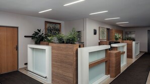 A reception area with wooden reception desks, a black mat, and potted plants. - Ankora Hotel Prague (Prague)