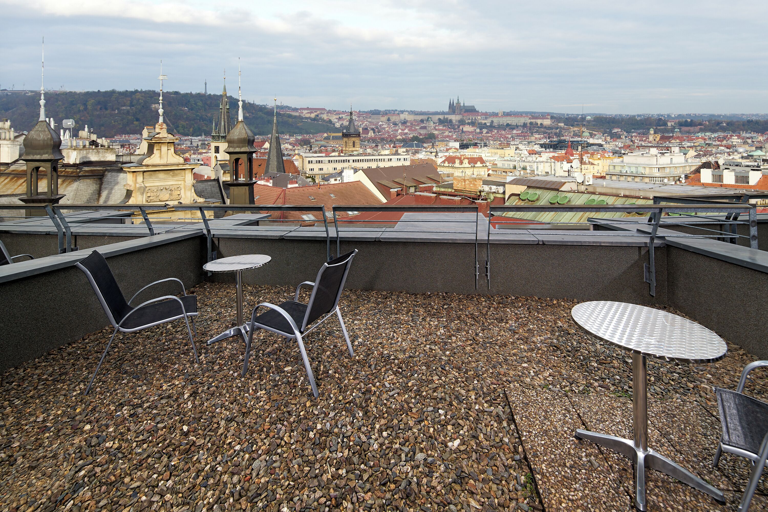 Terraza en la azotea con mesa y sillas, suelo de grava y vista panorámica de la ciudad al fondo.