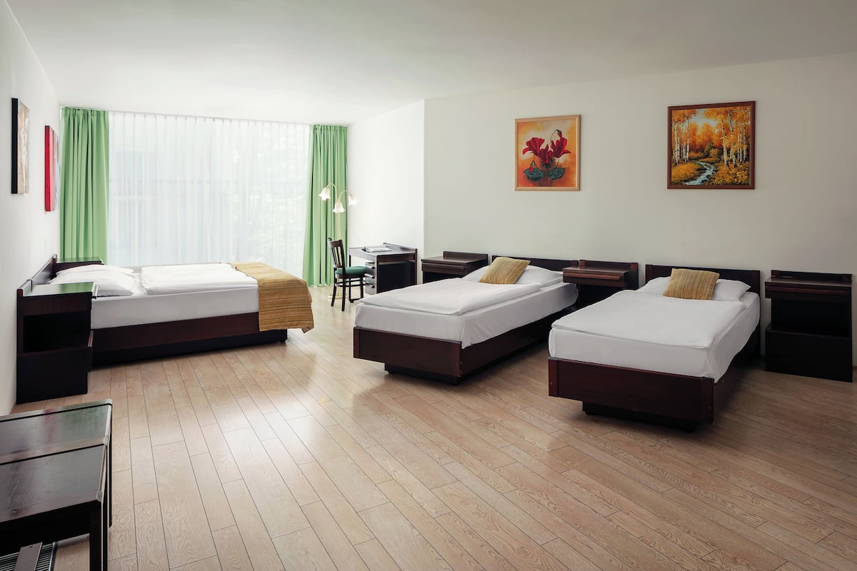 A hotel room with two single beds, a desk, a chair, and two paintings on the wall.