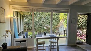 Uma sala de estar moderna com uma grande janela, uma mesa de jantar com duas cadeiras e um vaso de planta.