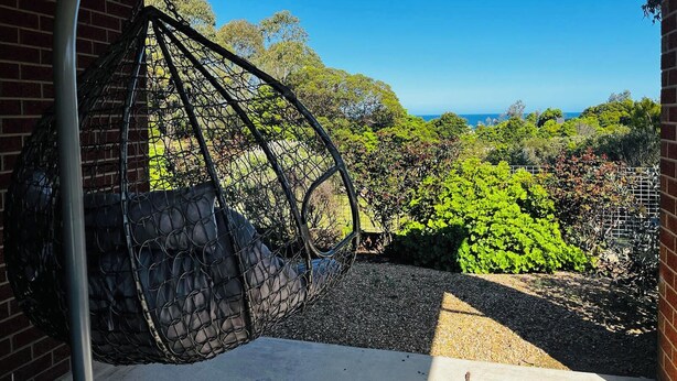 Una poltrona sospesa in un'area esterna coperta con vista sull'oceano e sul verde.