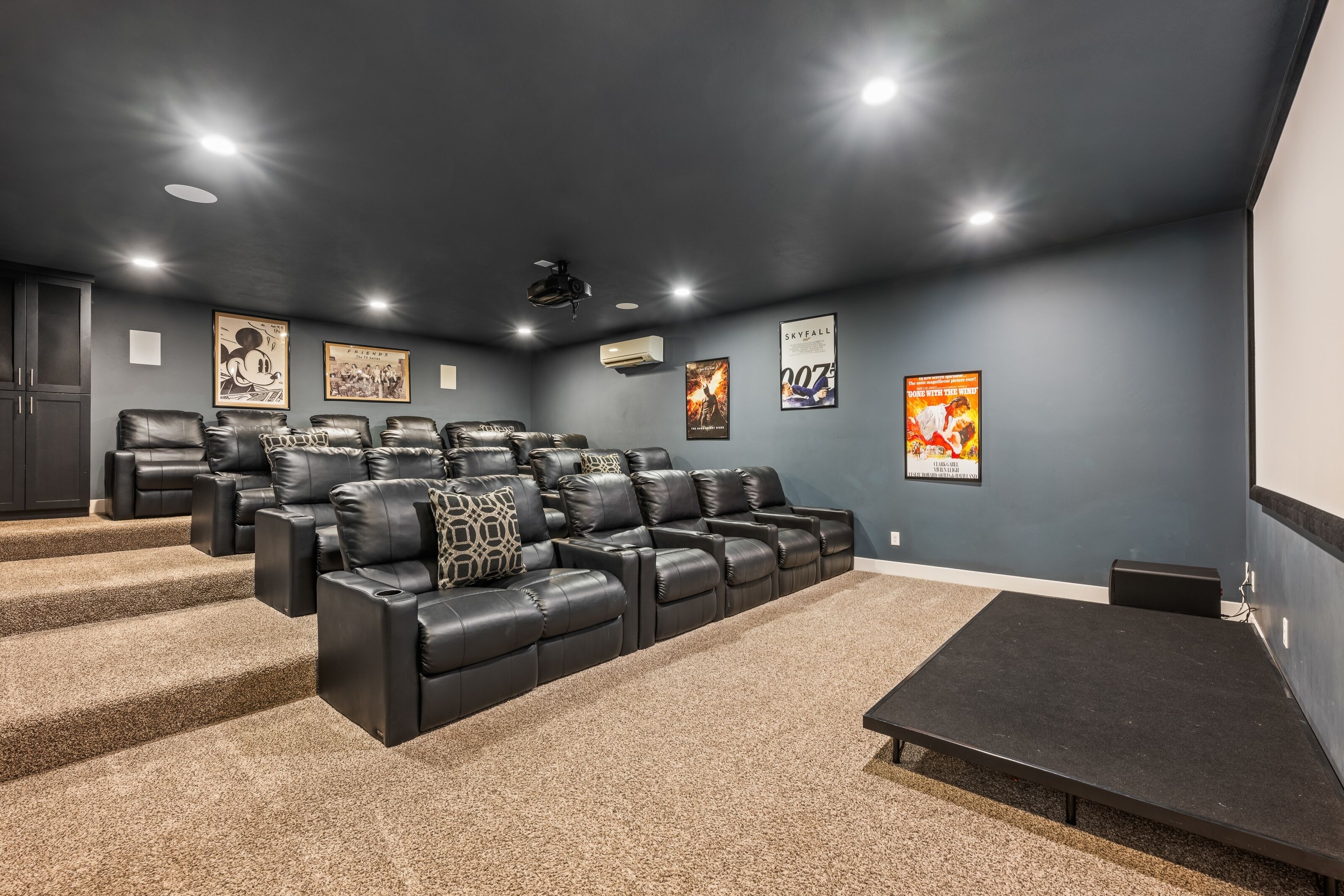 A home theater room with a black leather sectional sofa, a carpeted floor, and a projector screen.