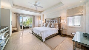 Ein geräumiges Schlafzimmer mit einem großen Bett, einem Deckenventilator, einem Schreibtisch und Blick ins Freie.