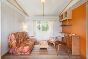 Ett kompakt vardagsrum med en soffa, ett litet bord, en stol, ett skåp och ett fönster med gardiner.