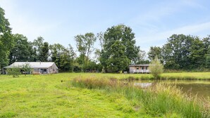 Un champ herbeux avec un étang, deux bâtiments en bois et des arbres en arrière-plan.