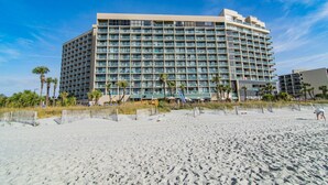 A large, multi-story hotel with a modern architectural design, located adjacent to a sandy beach with palm trees. - Gorgeous, Epic Ocean View, & Steps to Beach! Lazy River, Pools, HotTub! (Myrtle Beach)