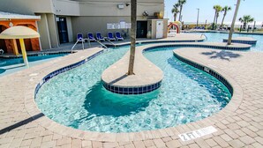 A swimming pool with a tree in the center, surrounded by lounge chairs and palm trees. - Gorgeous, Epic Ocean View, & Steps to Beach! Lazy River, Pools, HotTub! (Myrtle Beach)
