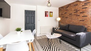 Ein modernes Wohnzimmer mit einem grauen Sofa, einem weißen Esstisch und einem schwarz-weißen Teppich.
