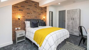 Ein Schlafzimmer mit einer Ziegelfassade, einem Bett mit gelber Decke, einem Kleiderschrank und einem Schreibtisch mit Stuhl.