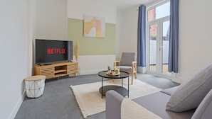 Un salon moderne avec un téléviseur à écran plat, un canapé gris, une table basse ronde et une fenêtre avec des rideaux.
