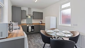 Une cuisine moderne avec des meubles gris, un four encastré et un coin repas comprenant une table en verre et des chaises noires.