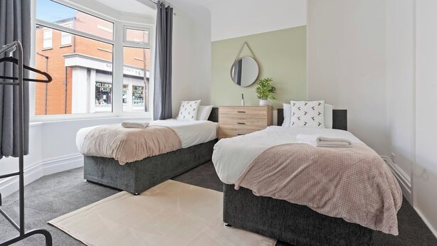 Une chambre moderne avec deux lits, une grande fenêtre, un miroir et une vue sur la rue.