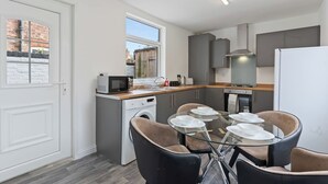 Une cuisine compacte équipée d’un lave-linge, d’un four à micro-ondes et d’un coin repas avec une table et des chaises en verre.